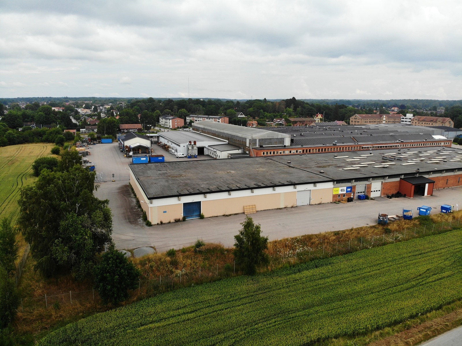 Flygbild över fastigheten på Fabriksvägen 33 i Mörrum, med lastkajer, industrihallar och omgivande åkermark.