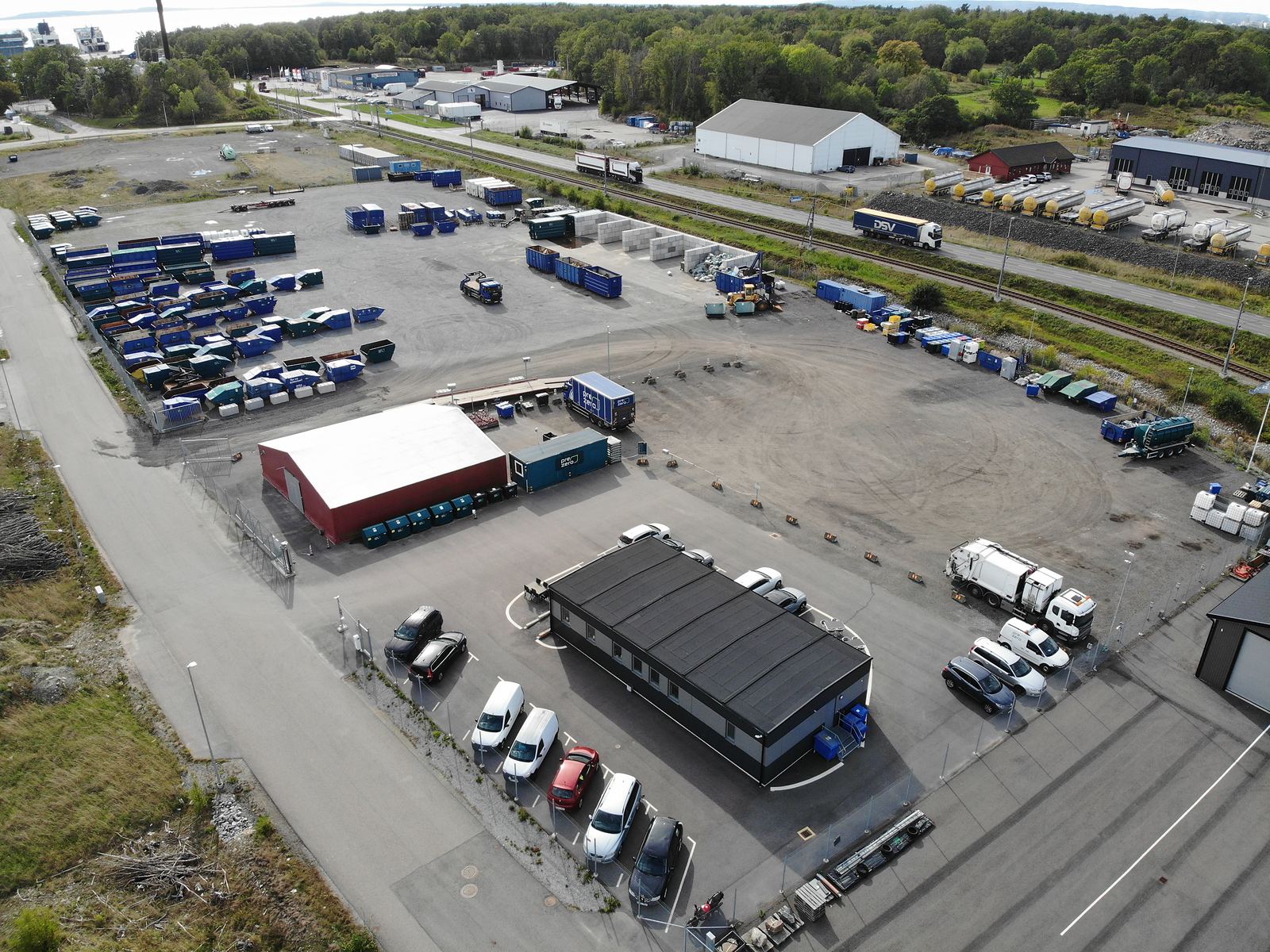 Flygbild över Östersjövägen 13-27 i Karlshamn med inhägnad asfaltsyta, kontorsbyggnad med parkering, lagerhall och containeruppställning, med järnvägen och hamnen bakom.