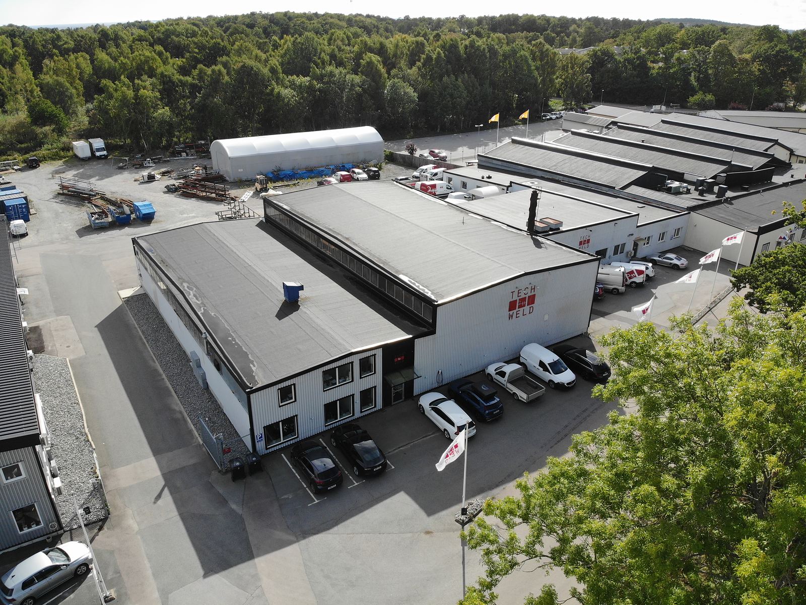 Kontors- och industrifastigheten på Pilvägen 6 i Karlshamn sedd från luften, med kontorsdelen i vinkel mot verkstadshallen, parkering på gården och grannfastigheterna i företagsområdet bakom.