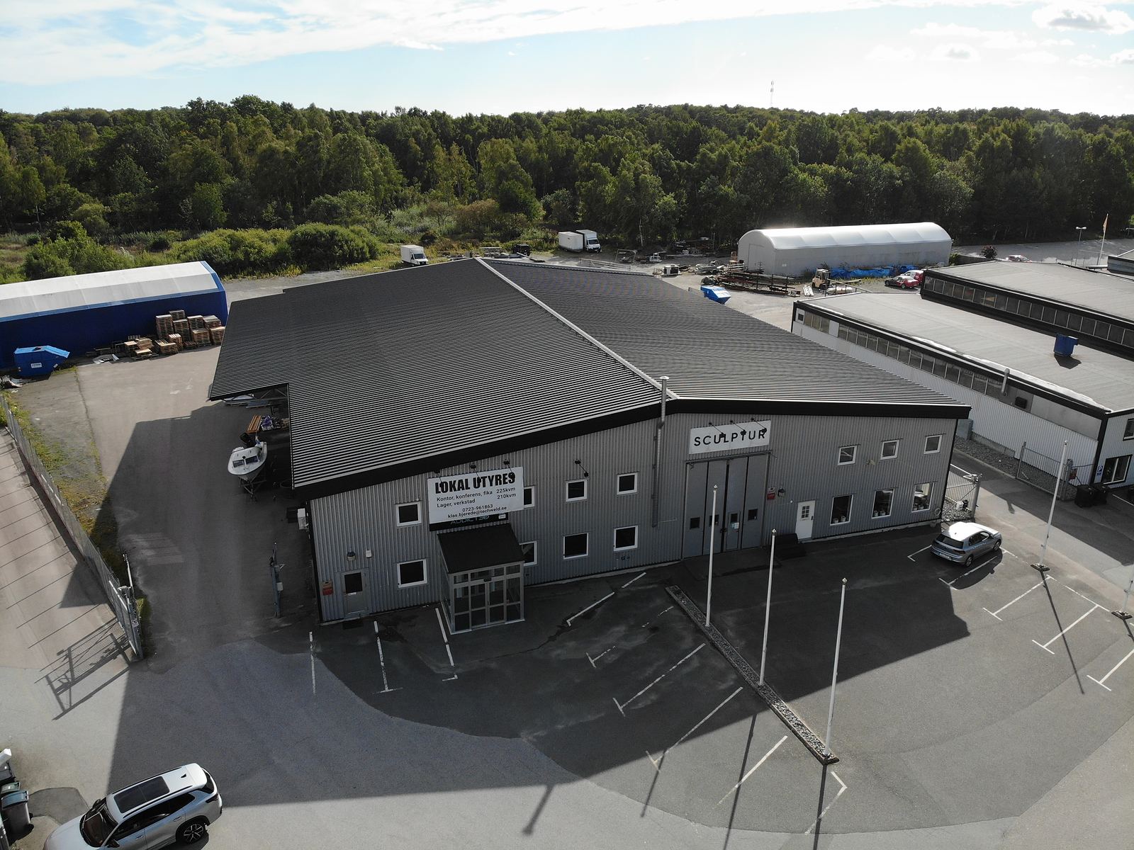 Fastigheten på Pilvägen 8 i Karlshamn sedd från luften, med skylten Lokal uthyres på långsidan, entrén mot parkeringen och gårdsytan runt om.